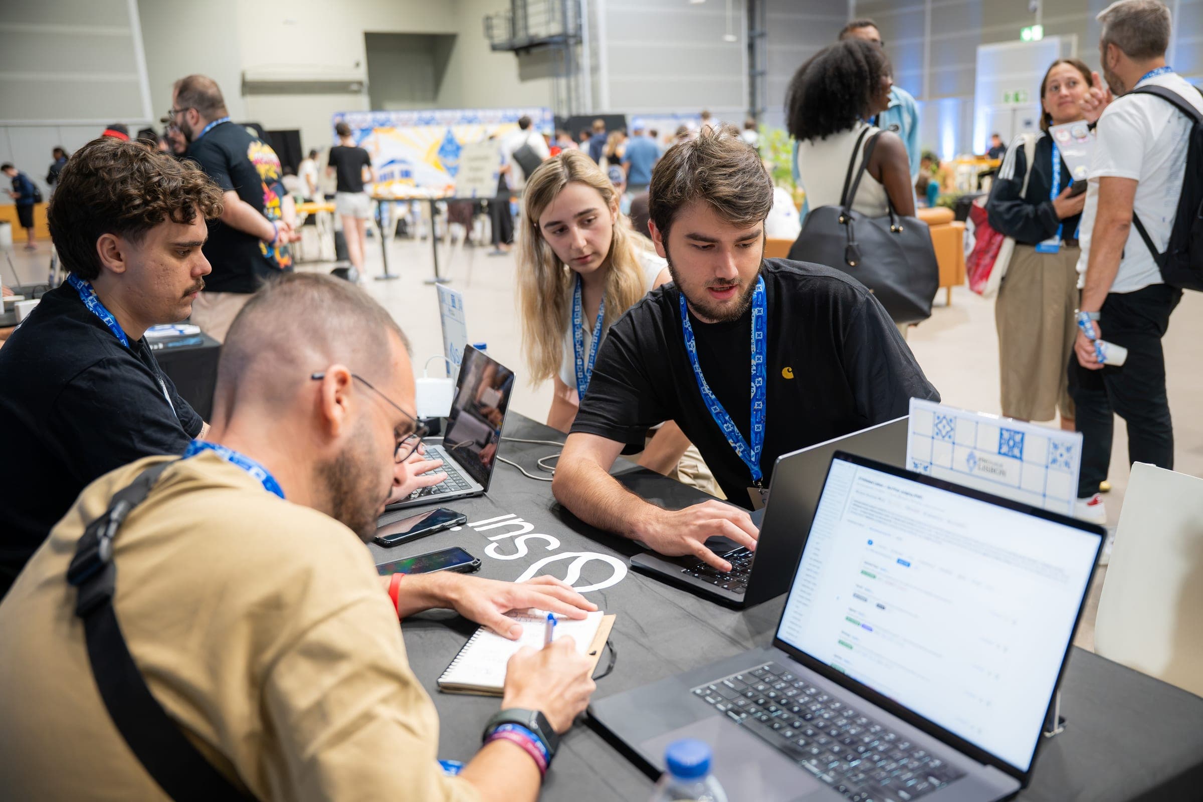 Builders work on laptops at the Sui table at ETHGlobal Lisbon while a mentor takes notes.